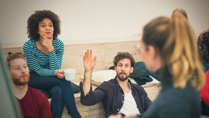 people in casual meeting with man raising his hand