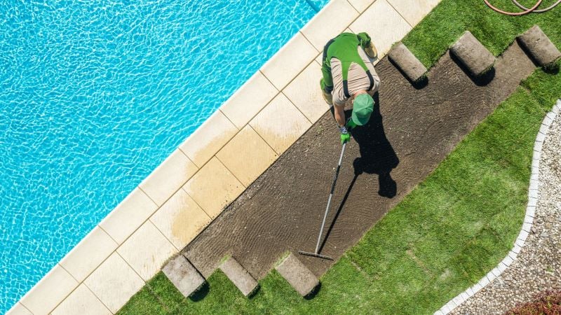person laying down turf near pool