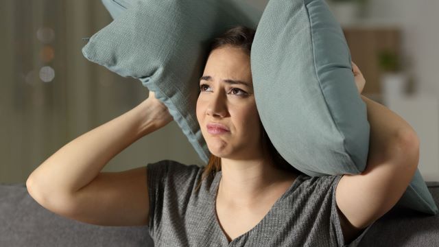 Woman with pillows on her ears to block out neighbor's noise
